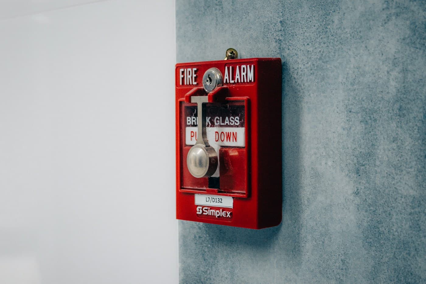 An installed red Simplex fire alarm pull station with its device identification label visible.